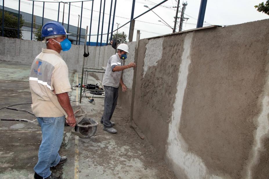 dois homens realizam trabalho em muro de escola #paratodosverem