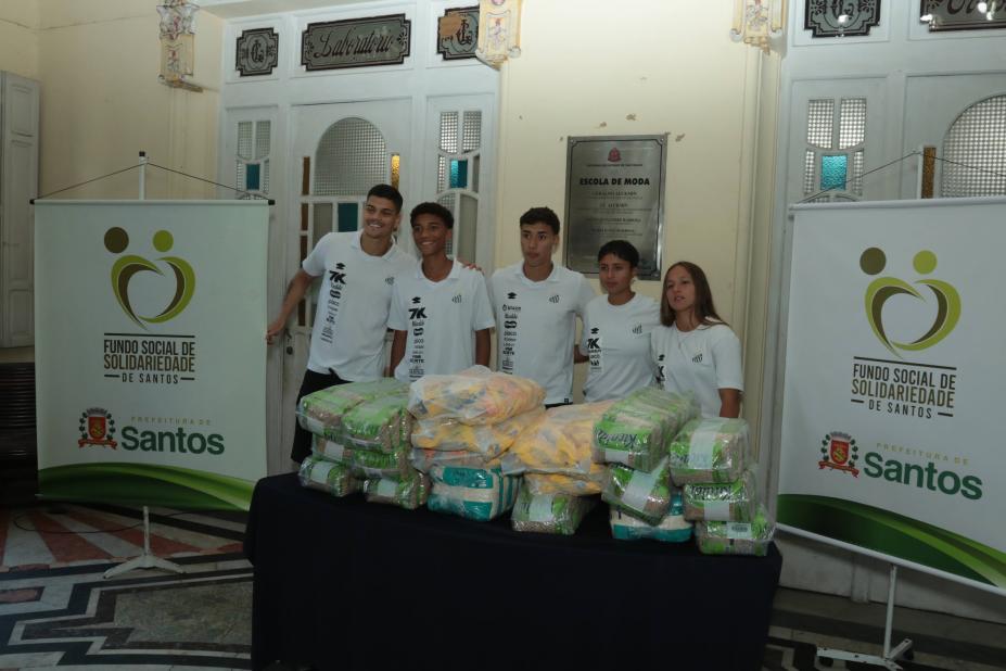 atletas do santos posam para foto atrás de mesa com mantimentos. #paratodosverem