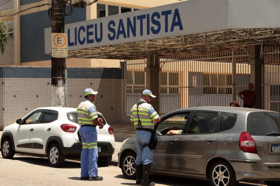 dois agentes de trânsito estão próximo a um carro que está parado na porta de uma escola. #paratodosverem