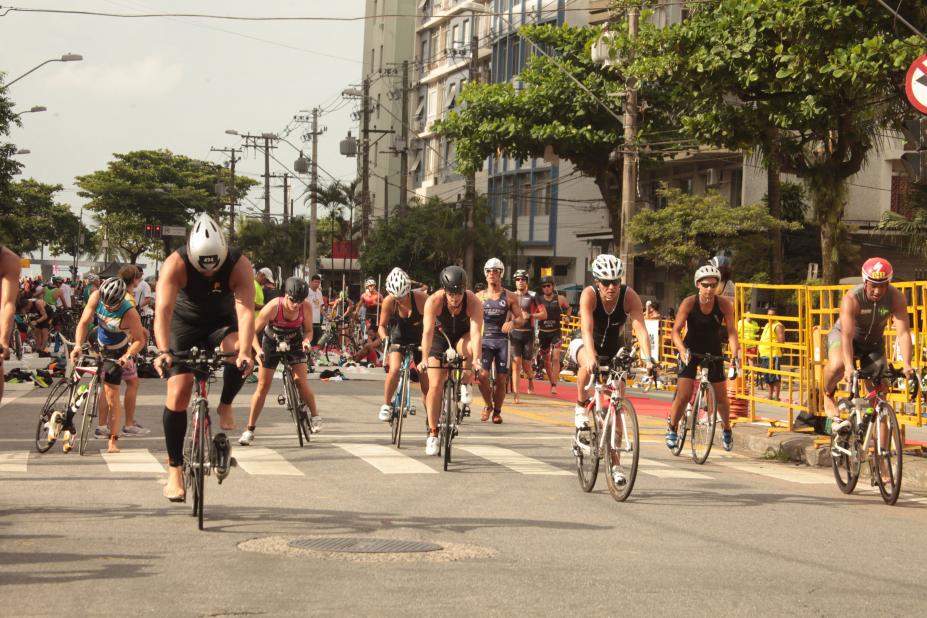 Ciclistas estão pedalando em avenida. Todos estão usando capacete. #Pracegover