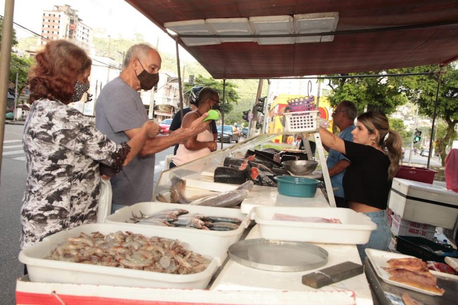 pessoas comprando peixe em barraca localizada em rua #paratodosverem