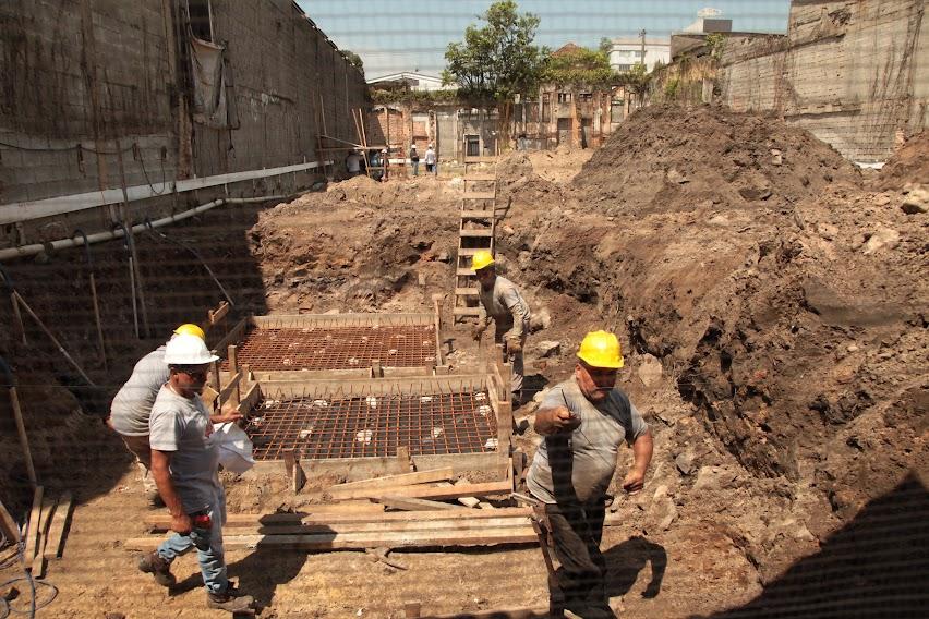 homens estão trabalhando em terreno. eles mexem em estruturas de ferro. #paratodosverem