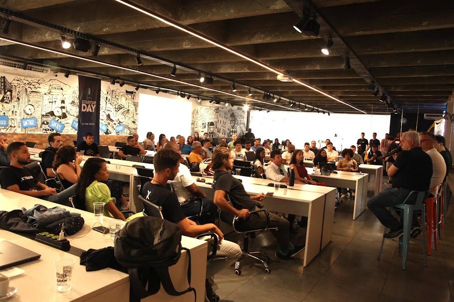 jovens e adultos estão sentados em um salão assistindo palestra. #paratodosverem