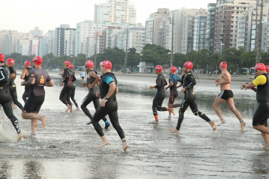atletas com uniformes de natação estão entrando no mar na praia de Santos. #paratodosverem 