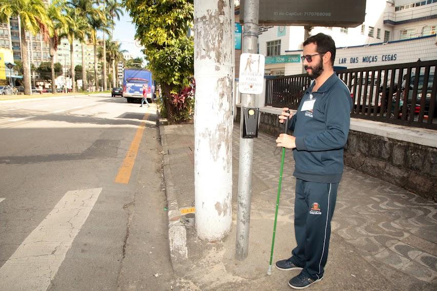 homem está ao lado de botoeira em poste pronto para fazer a travessia de pedestres. #paratodosverem