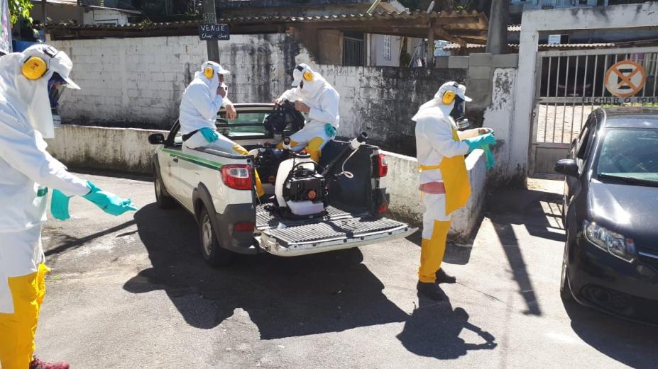 Homens paramentados com aventais, roupas, gorros e máscaras se prepararam para nebulização. #paratodosverem