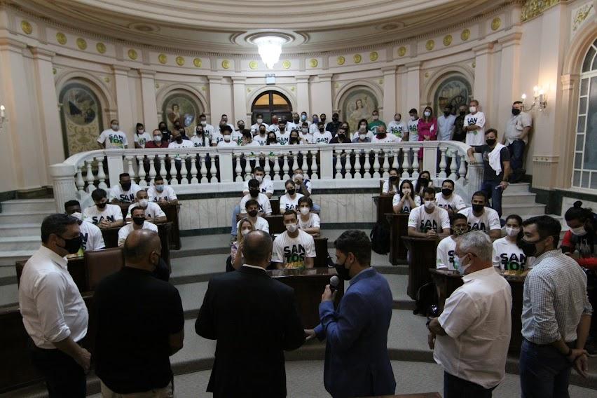 Autoridades discursam em pé para atletas sentados na galeria da Sala Princesa Isabel. #pracegover