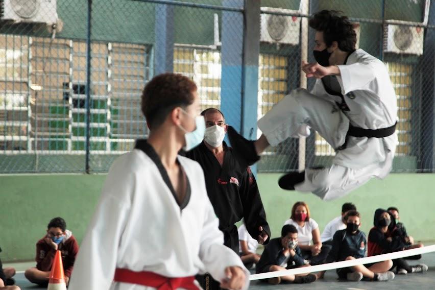 Mestre e atleta observam lutador executando golpe no alto #paratodosverem