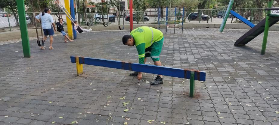 peça é removida de playground por homem. Ao fundo, uma criança brinca em balancê. #paratodosverem