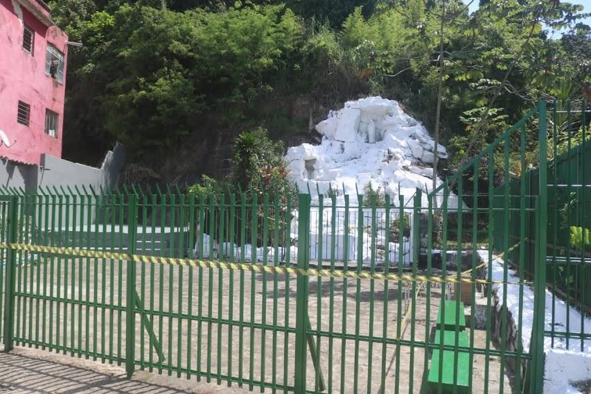 a gruta ao fundo, encostada o morro, e o gradil da praça em primeiro plano. #paratodosverem