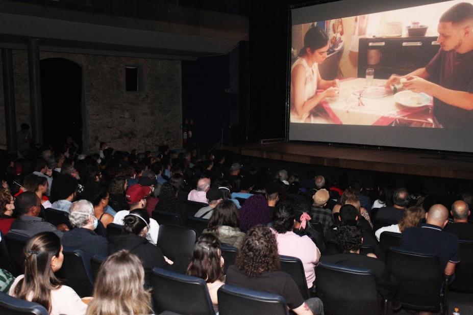 plateia lotada assistindo a filme projetado na tela. #paratodosverem