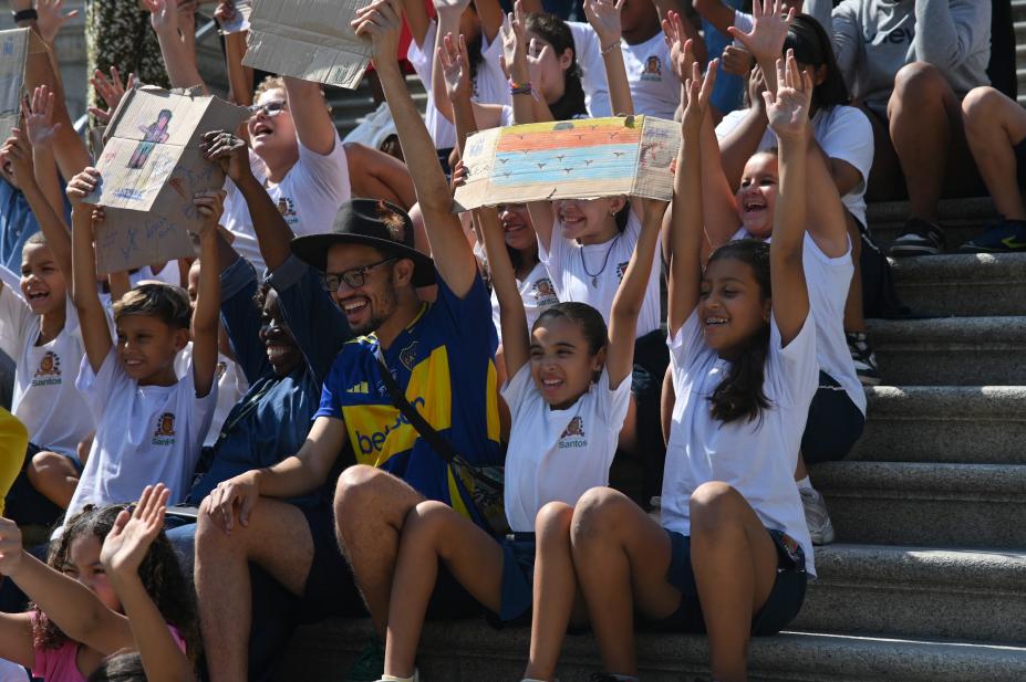 preo e criaças seguram desenhos nas mãos no alto da cabeça. #paratodosverem 