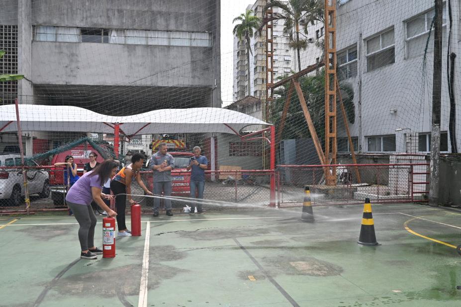 duas pessoas seguram extintos emitindo jato para ponto sinalizado em quadro em simulação para apagar incêndio. #paratodosverem