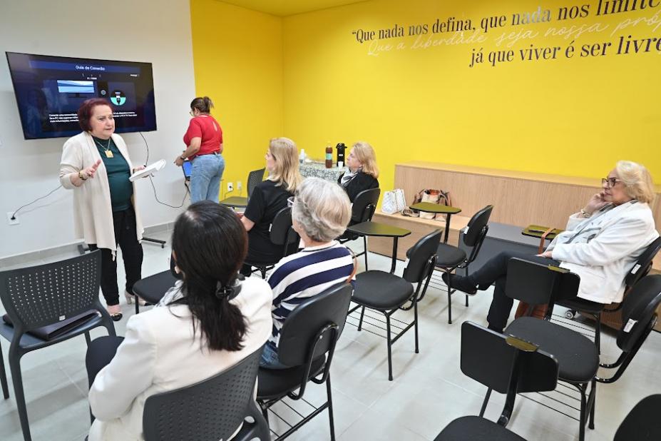 mulher em pé fala a outras que estão sentadas. #paratodosverem