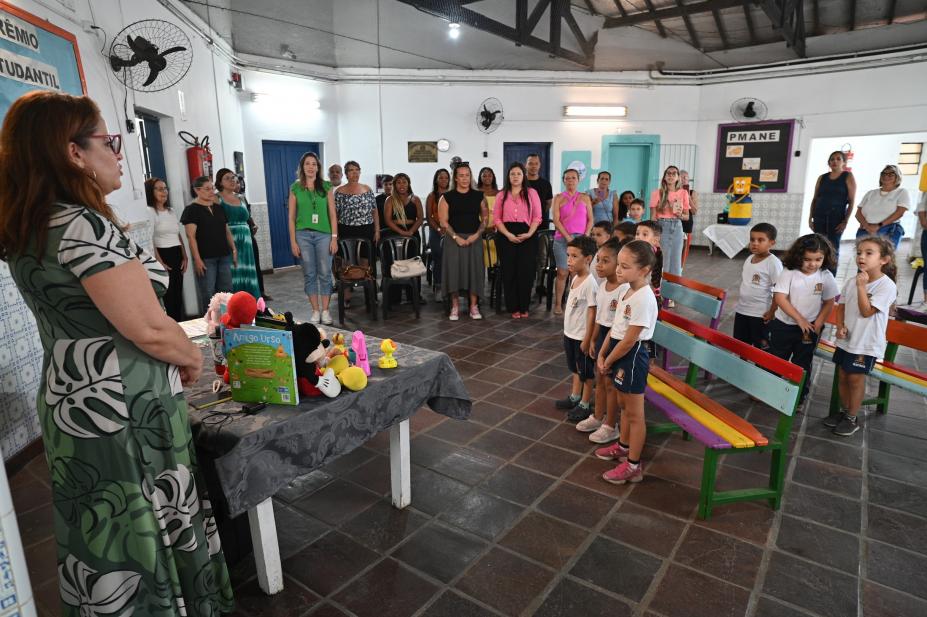 pátio de escola com crianças e adultos em pé para evento solene. #paratodosverem