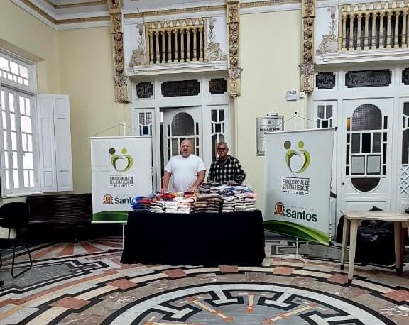 mesa com donativos e dois homens atrás. #paratodosverem