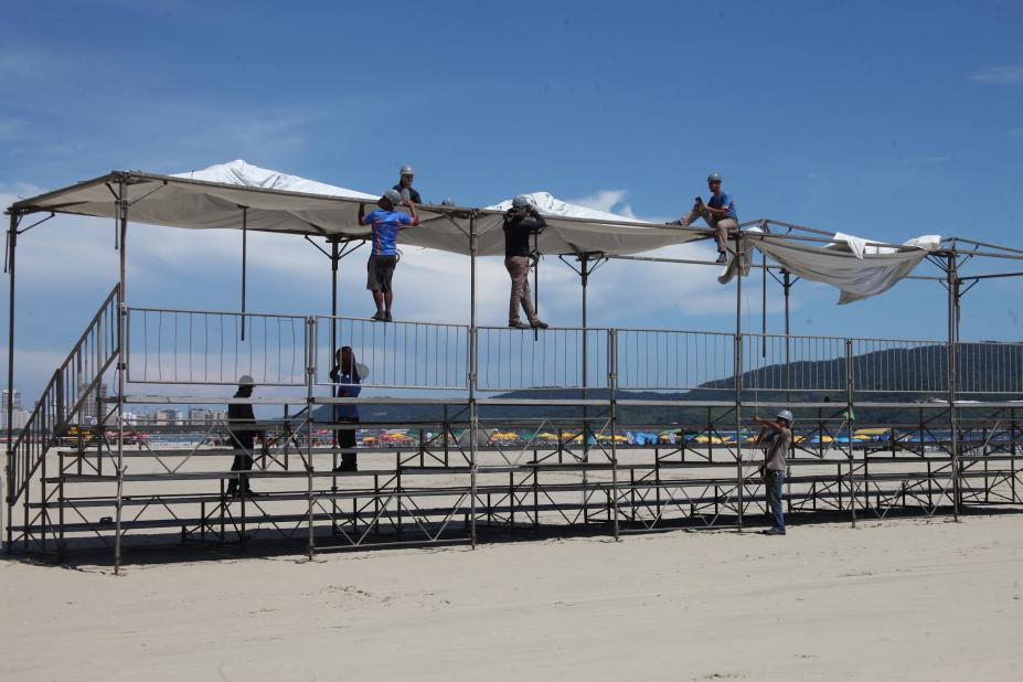 homens montam estrutura de arquibancada sobre a areia. #paratodosverem 