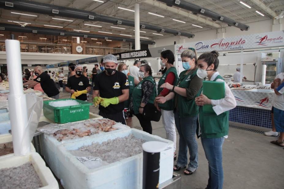 Fiscais uniformizados estão diante de caixas de pescado. #Paratodosverem