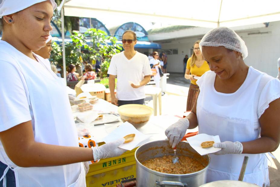 Mulheres retiram de panela creme de camarão para recheio de massa servida ao público em guardanapos