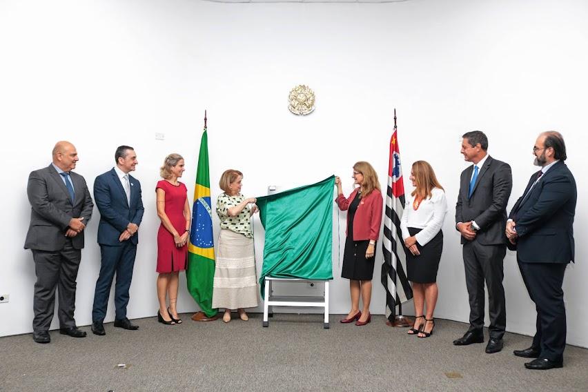 oito pessoas descerram placa. Atrás delas estão a bandeira do Brasil e a do Estado de São Paulo. #paratodosverem