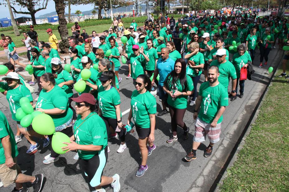 Pessoas vestidas com camisetas verdes caminham pela avenida da orla. #Pracegover