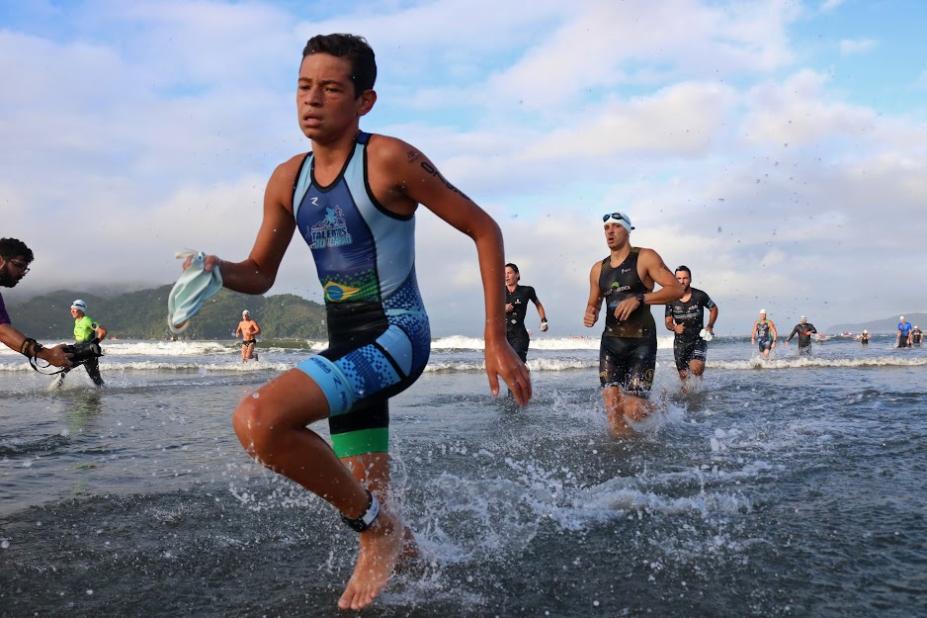 jovem está saindo da água, na beira do mar, encerrando prova aquática. #paratodosverem