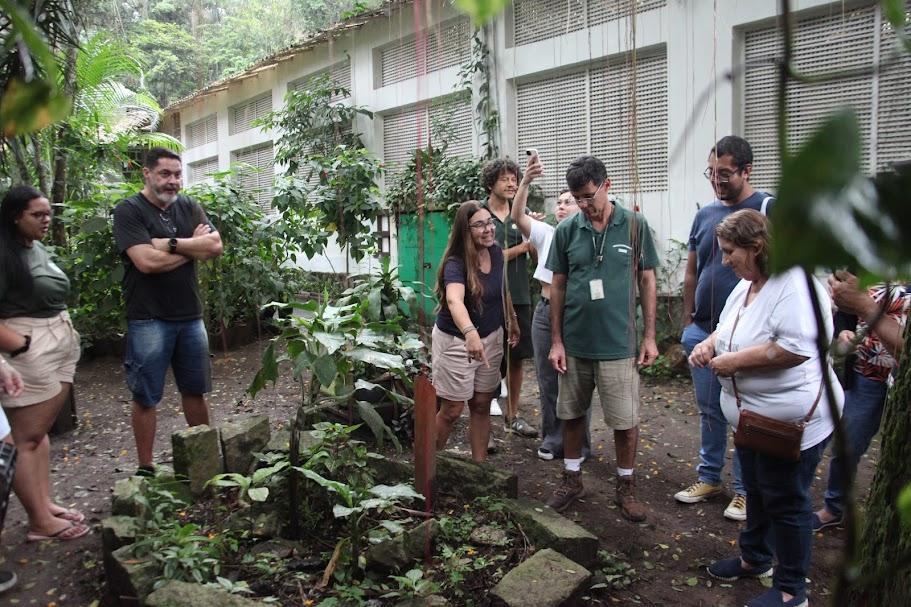 grupode pessoas está em volta de uma composta e uma área verde. #paratodosverem 