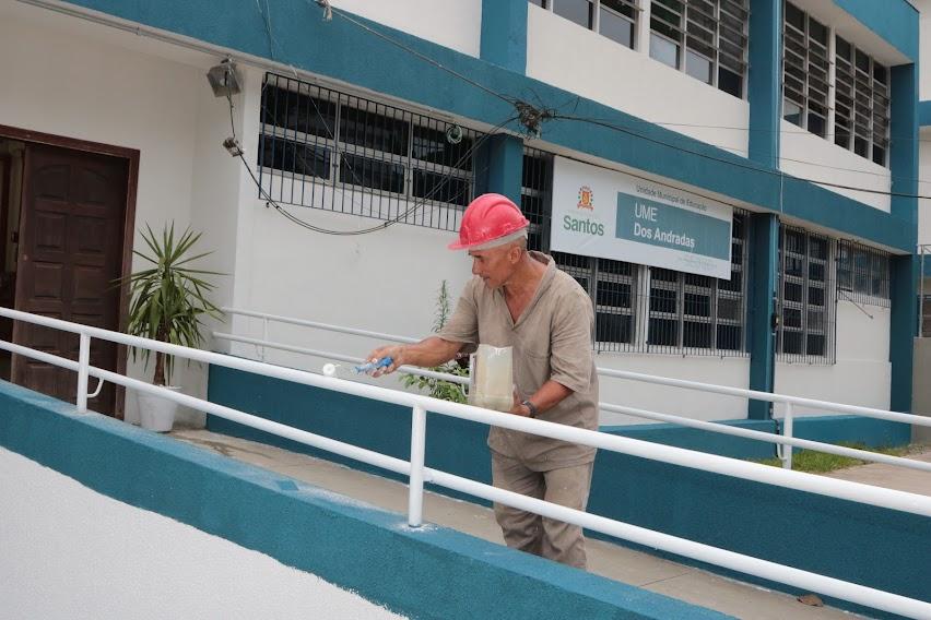 homem está pintando corrimão de rampa de acesso à escola. #paratodosverem