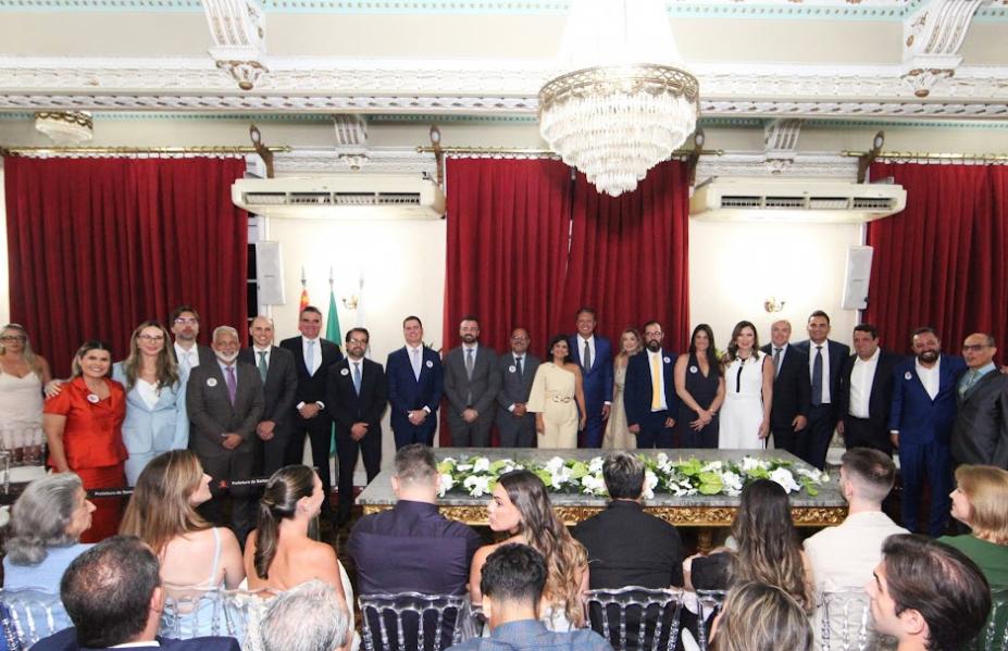 secretários, vice prefeita e prefeito em pé, posam para foto em auditório, com público sentado. #paratodosverem 
