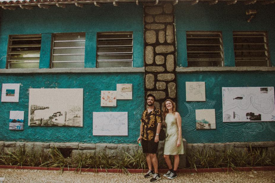 um homem e uma mulher estão à frentne de quadros expostos no muro da fachada do aquário. #paratodosverem 