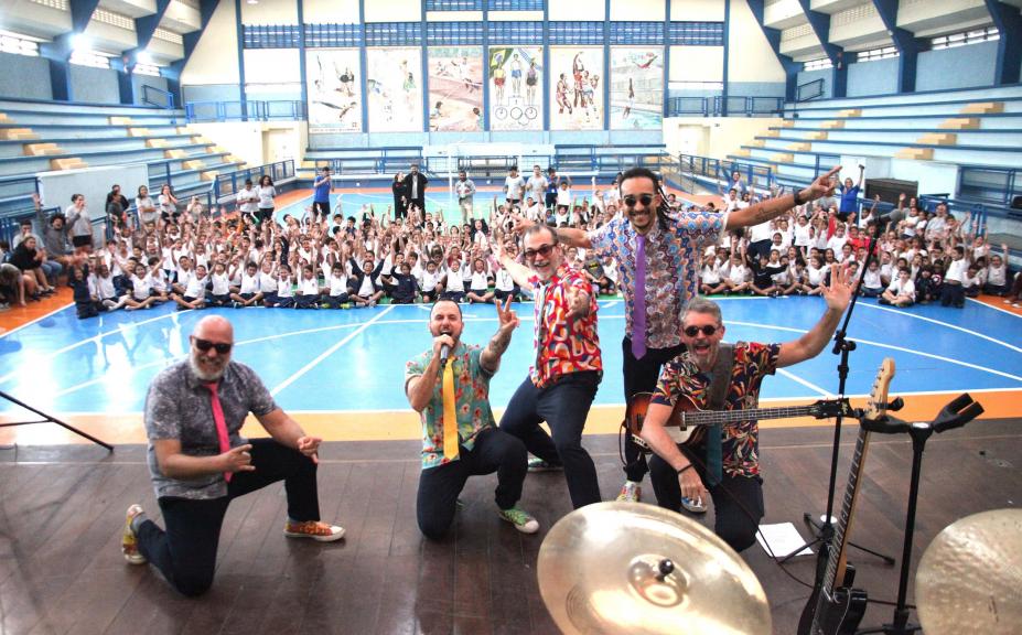 músicos fazem pose para fotos com crianças ao fundo. #paratodosverem