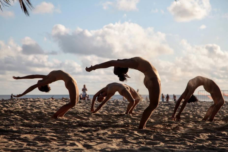 bailarinas dançam na areia e tem o tronco curvado para trás em busca de atingir o chão com as mãos. #paratodosverem