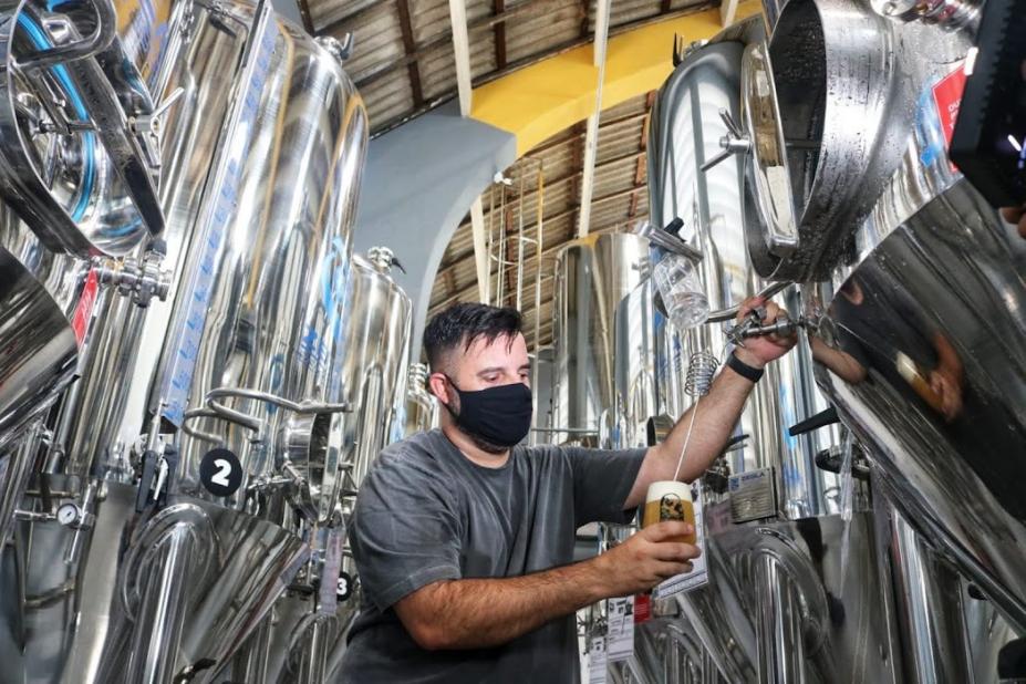 homem tira cerveja de equipamento na fábrica #paratodosverem