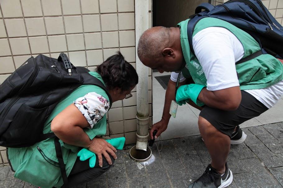 dois agentes de combate à dengue vistoriam saída de cano de água para ralo. #paratodosverem