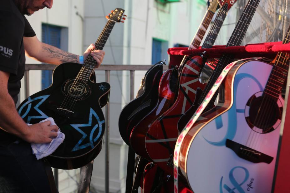 guitarras postas lado a lado. HOmem segura e limpa uma delas. #paratodosverem 