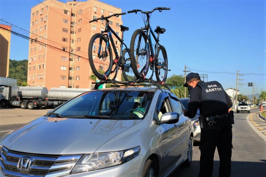 #pracegover Em avenida, guarda aborda motorista de carro com bicicletas na capota