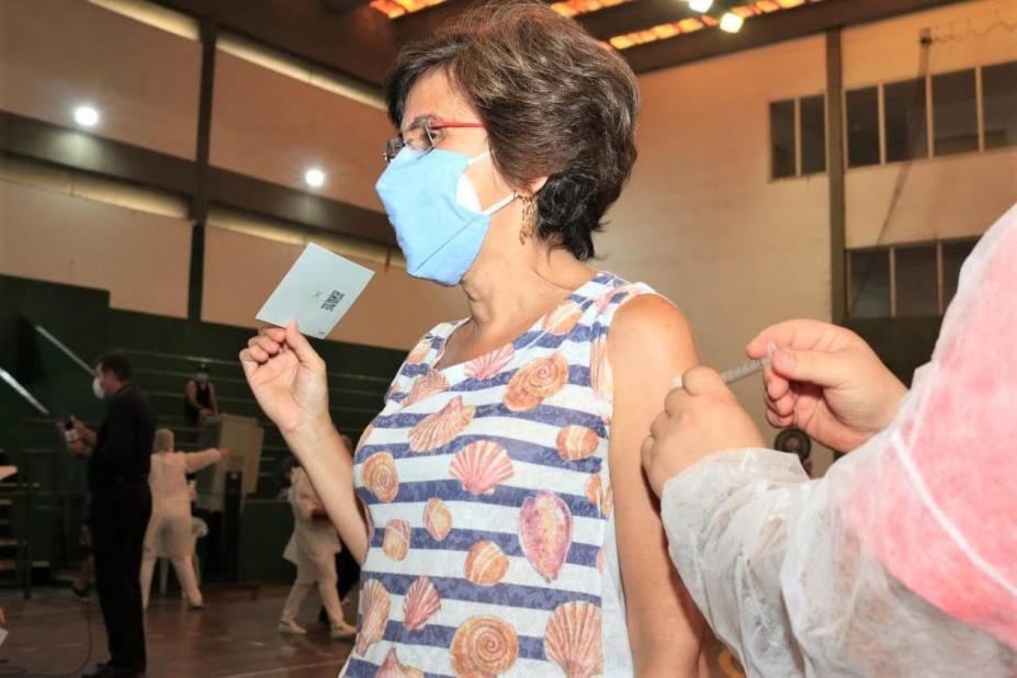 Mulher com máscara facial recebe injeção de vacina no interior de ginásio