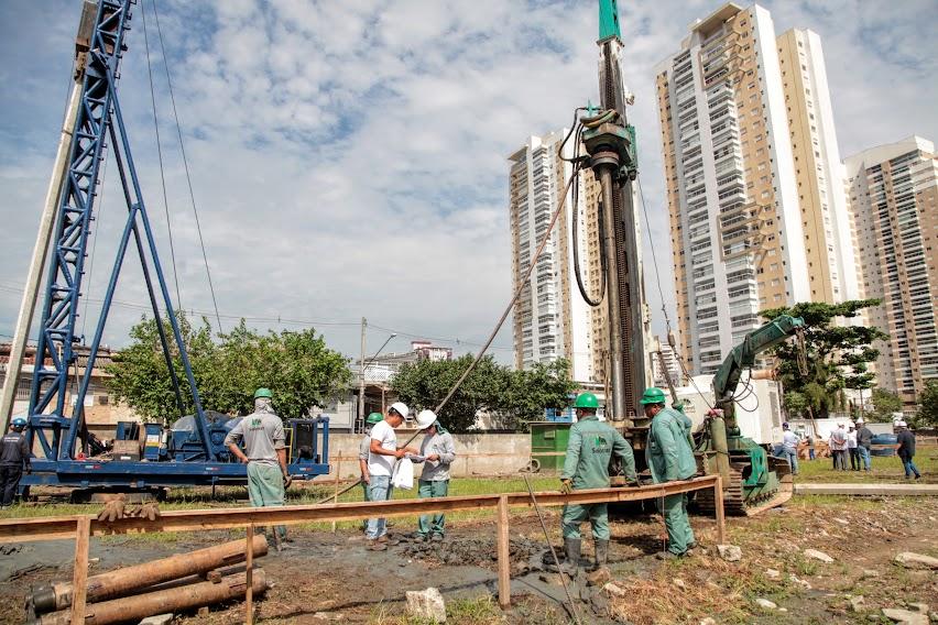 homens estão trabalhando em canteiro de obras em meio a máquinas de fundação. #paratodosverem