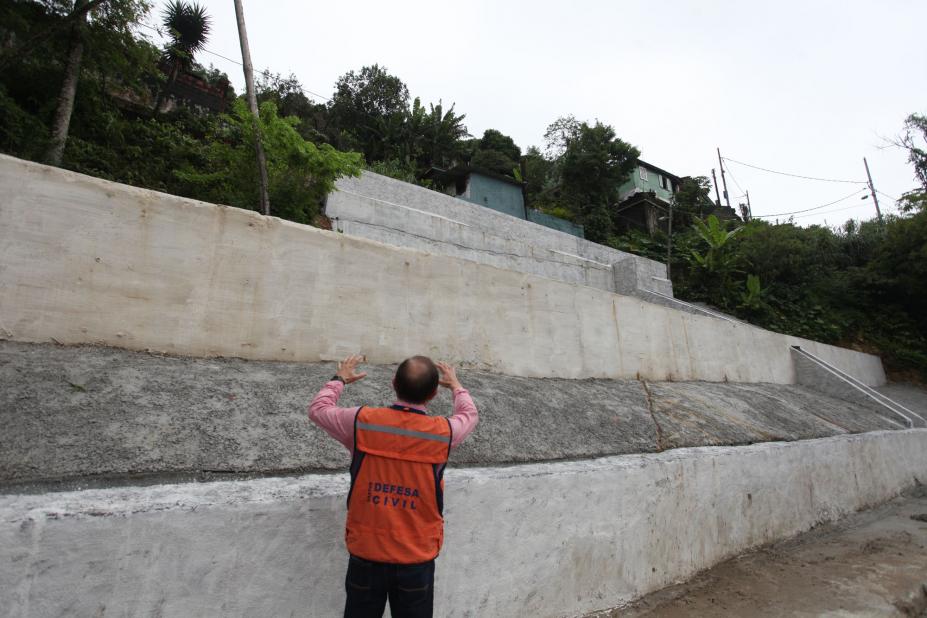 Grande muro arrimo em encosta. HOmem está na frente de costas para a imagem. #Pracegover