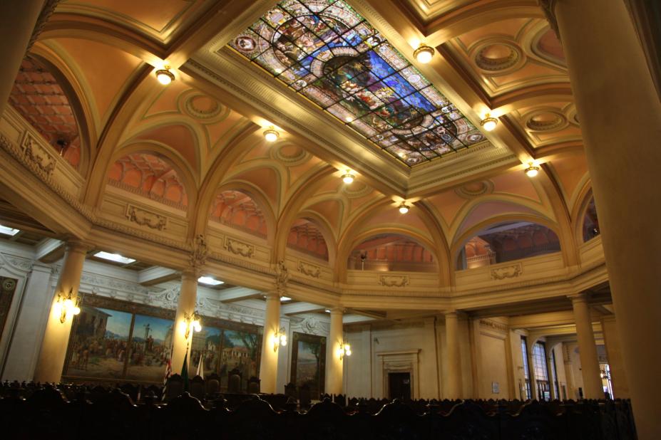 Interior do prédio da antiga bolsa do café, fotografado de baixo para cima. O teto com vitral está em evidência. #Pracegover