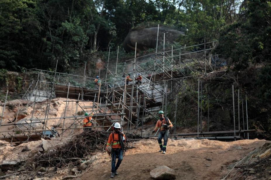 homens estão trabalhando em encosta onde foram instalados andaimes. #paratodosverem