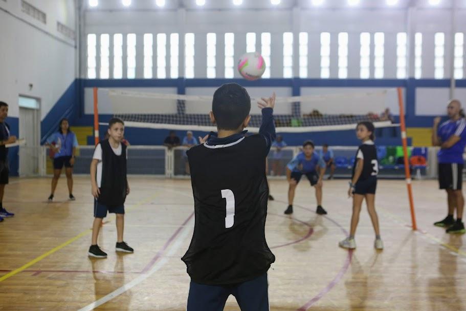 menino de costas para a foto está no início da quadra lançando a bola para o outro lado da rede. #paratodosverem 