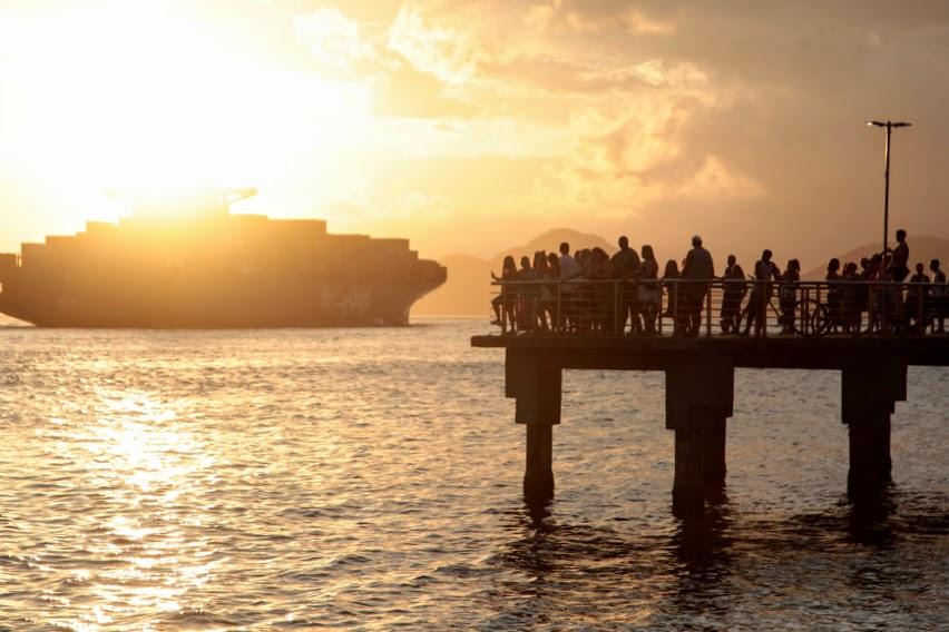 pessoas estão no deck do pescador vendo saída de navios. #paratodosverem 