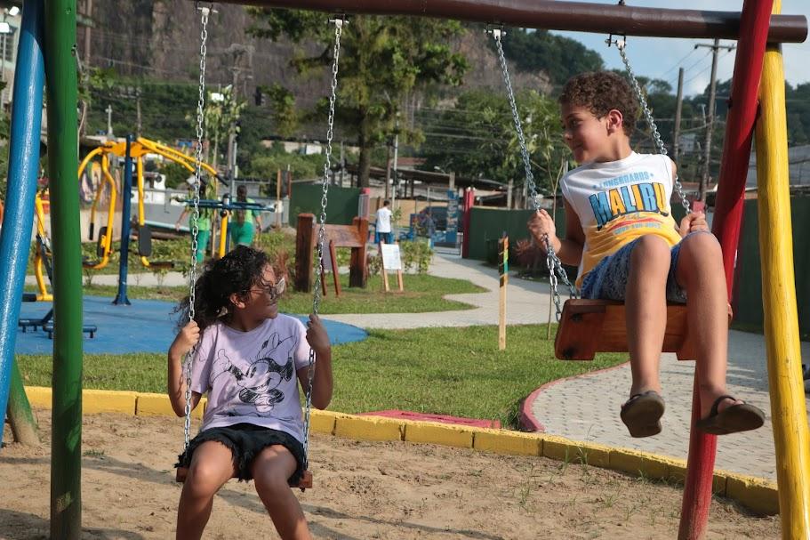 duas crianças brincam de balance. O menino, à direita está no alto. #paratodosverem 