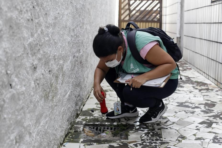 agente agachada olha para ralo com uma lanterna #paratodosverem