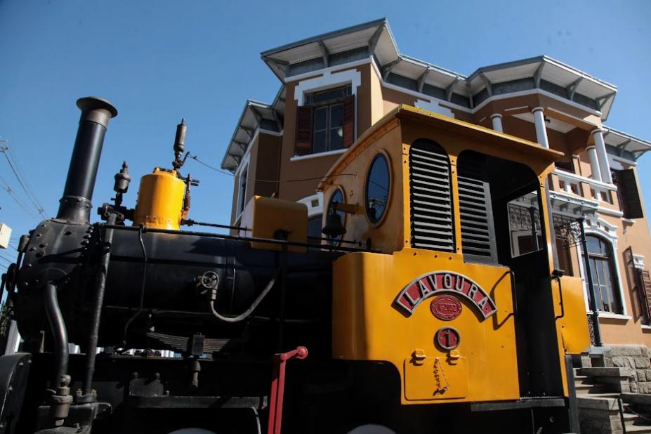 antiga locomotiva parada na frente de prédio. #paratodosverem 