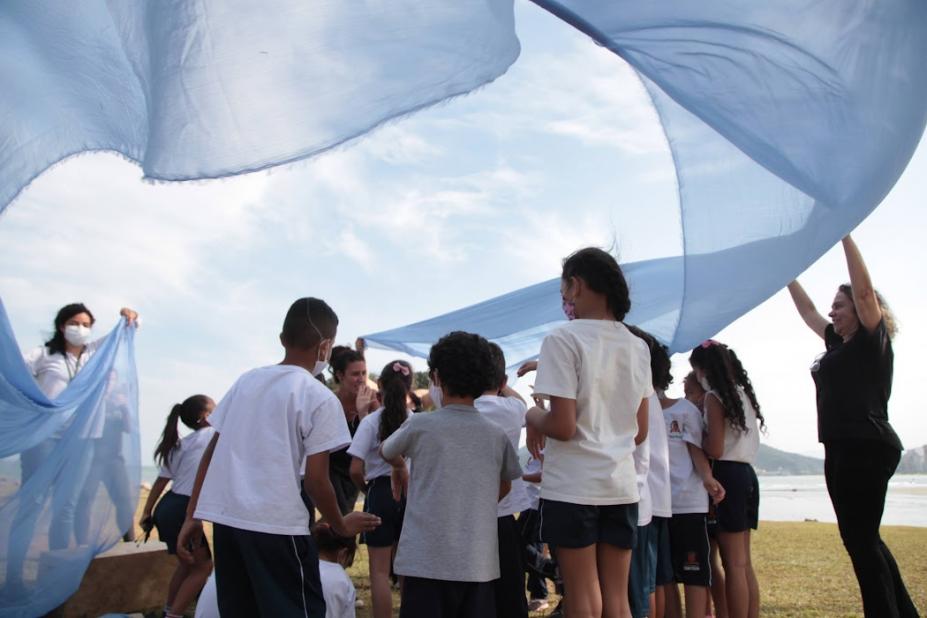crianças brincam em jardim envoltas de pano azul #paratodosverem