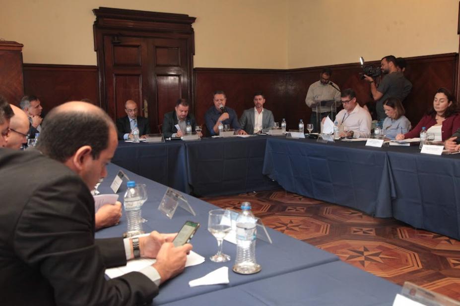 reunião com diversas pessoas sentadas em mesa em formato de U. #paratodosverem 