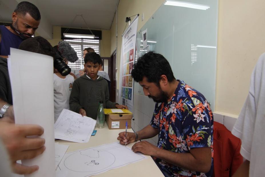 Artista peruano faz desenho observado por estudantes. #paratodosverem