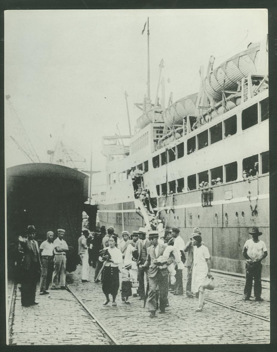 Imagem antiga. Japoneses desembarcam em Santos. Navio está encostado no cais. #Pracegover